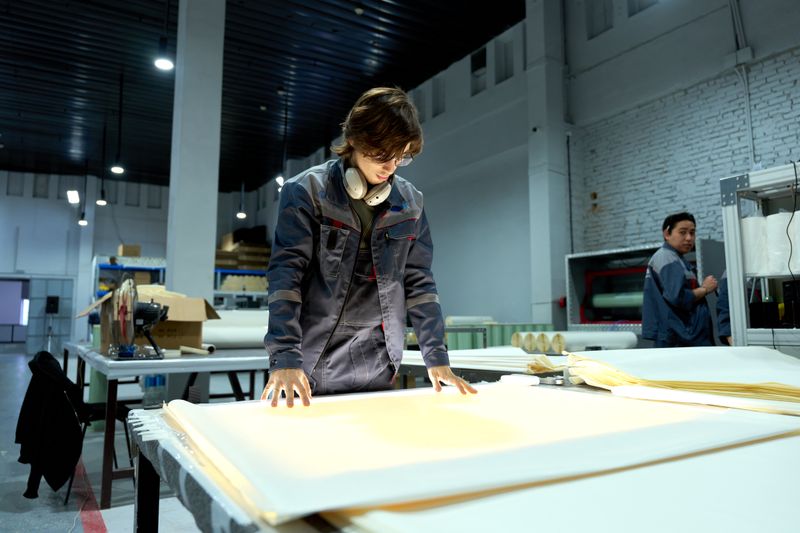 Worker in uniform examining sheets in a brightly lit factory environment, focusing on quality