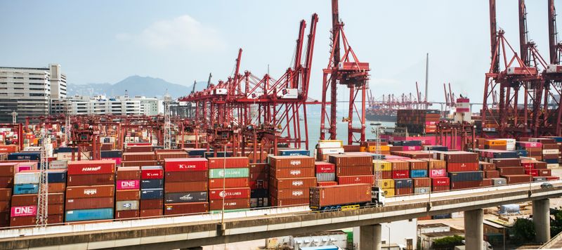 A bustling scene of cargo containers and cranes at a Hong Kong port, showcasing global trade