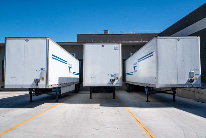 Three white cargo trailers parked at an industrial shipping dock under clear blue skies